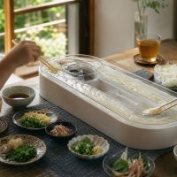 家庭の食卓に置かれた流しそうめん機でそうめんを取る様子