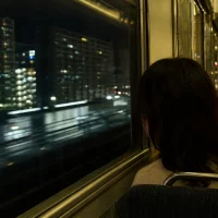 夜の大阪環状線の車内から夜景を眺める後ろ姿