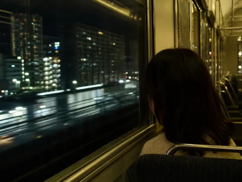 夜の大阪環状線の車内から夜景を眺める後ろ姿