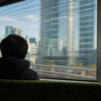 山手線の車内から昼の都心のビル群を眺める後ろ姿
